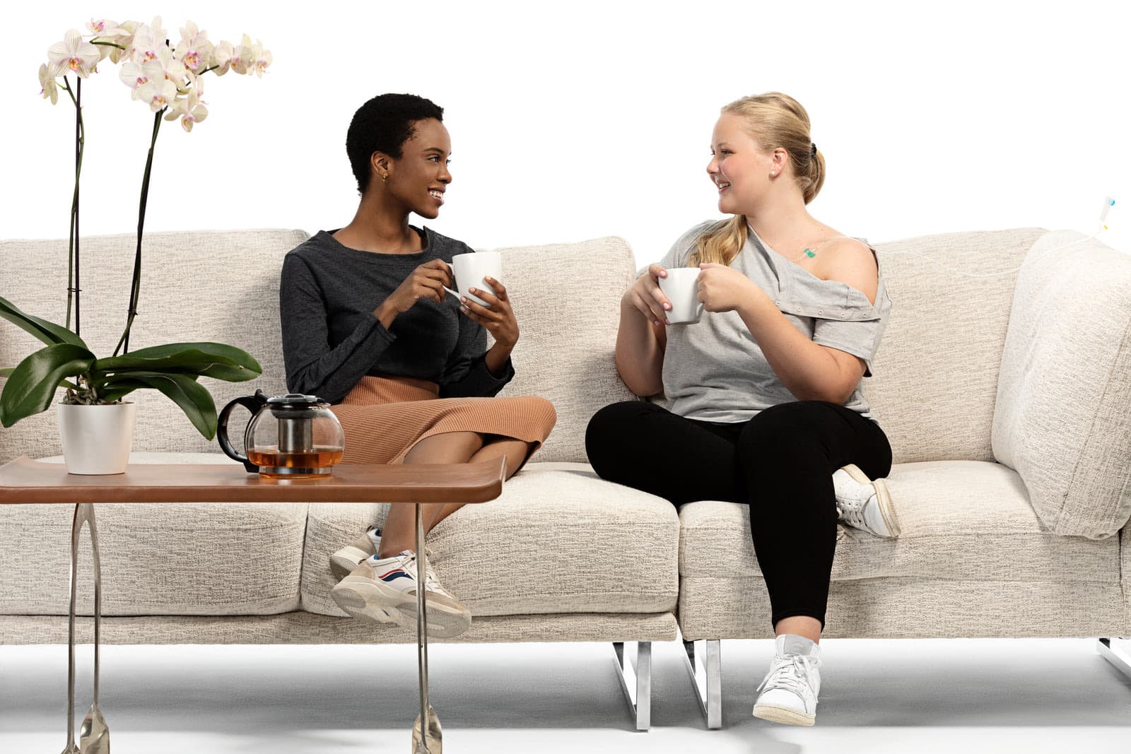 Two women in MAI We Care adaptive clothing sharing tea on a sofa
